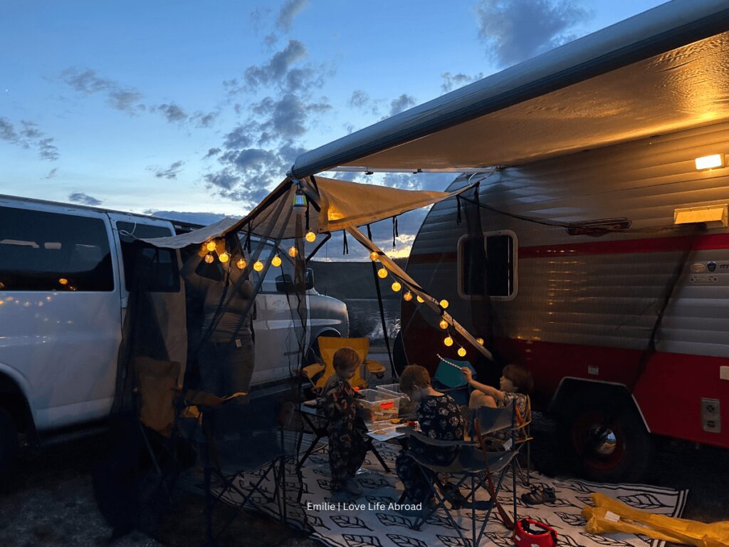 A nice family camping set up with lights, a rug and a bug net between two small campervan